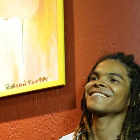 Robson POETA sorrindo junto a uma obra de sua autoria